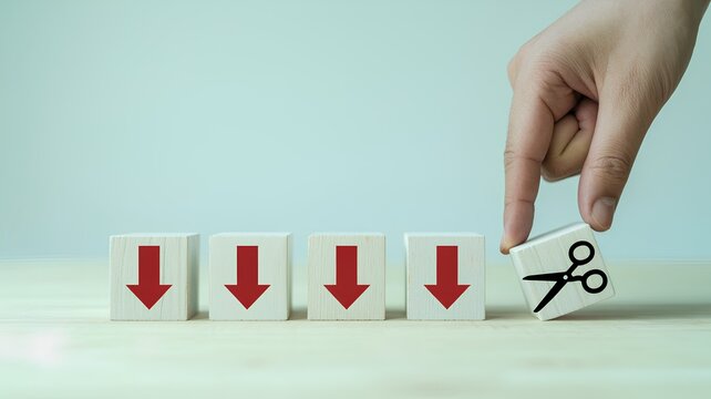 A hand holding scissors cutting a wooden block with a red downward arrow, symbolizing cost reduction or budget cuts