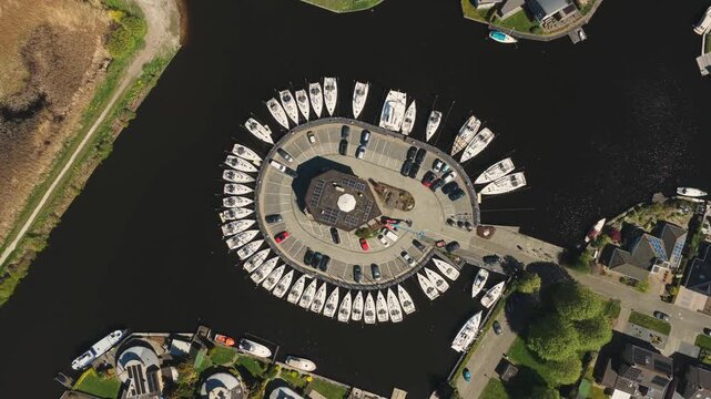 Aerial view of a unique circular marina with white sailboats docked around the perimeter and cars parked in the center in Lemmer, Friesland, Netherlands.