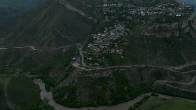 Drone footage of Gunib village on a high mountain plateau with winding road and dramatic ridges under clouds, Dagestan Republic, Russia, Caucasus Mountains
