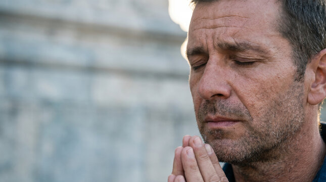 Close-up of a man praying with closed eyes near a historic stone monument, capturing a moment of serene reflection in soft natural light
