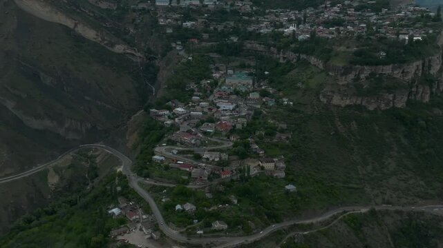 Drone aerial view of Gunib aul on a rocky plateau with winding road and steep cliffs, mountain landscape at dusk in Dagestan, Russia, Caucasus region