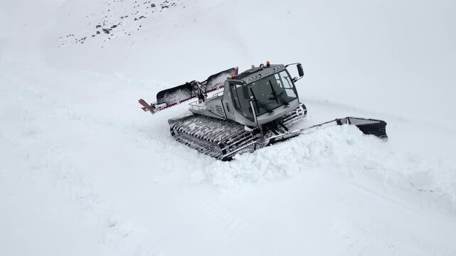 Snow groomer and snow cannon working on a ski slope.