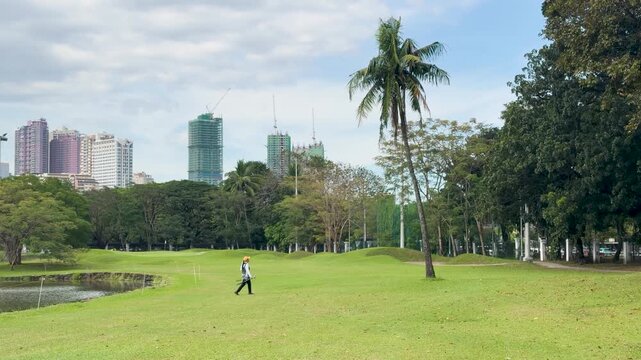 Filipino Golf Caddy Walking Across Green Fairway with Manila Skyline