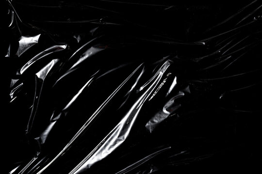 Transparent plastic wrap texture with wrinkles and glossy reflections on black background.