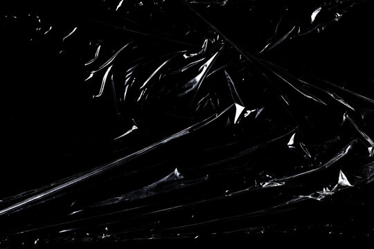 Transparent plastic wrap texture with wrinkles and glossy reflections on black background.
