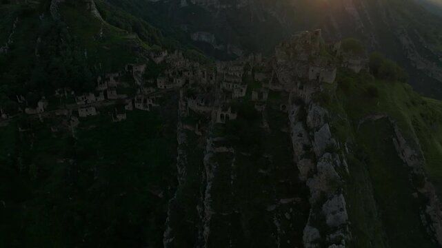 Drone footage of the abandoned aul of Gamsutl on a steep mountain ridge at golden hour, dramatic Caucasus landscape in Dagestan, Russia with sun flare