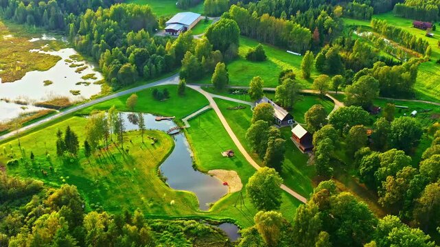 Lush green land featuring small lakes in aerial view with golden hour sunlight in Latvian countryside