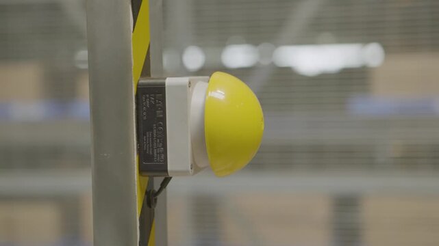Industrial safety button being pressed on striped pole in warehouse environment