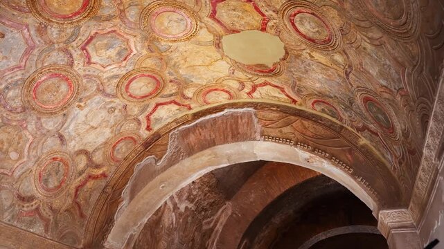 Ornate Pompeii vaulted ceiling with circular fresco motifs, decorated arch, and painted plaster, revealing a richly preserved Roman interior chamber.