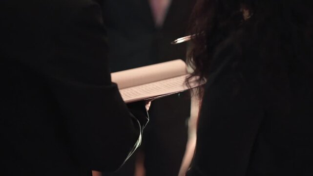 Person holding printed guest list while verifying names at event entrance with low light background and shallow depth of field during organized reception access control, close up shot