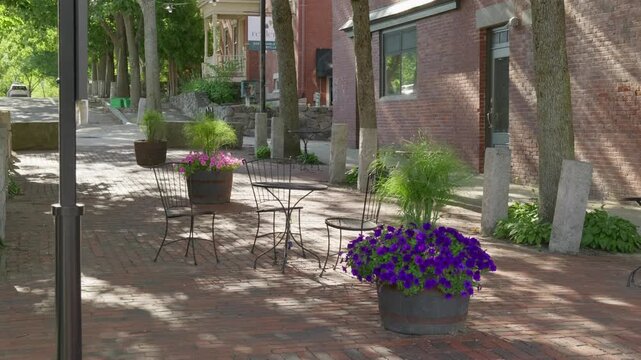 Static shot of a small brick patio in Dover, NH, USA. There is a small black bird on the ground and purple flowers in a planter next to the tables.