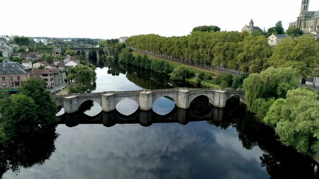 Medieval stone bridge with its arches reflecting in the calm waters of the Vienne in Limoges. Aerial plunging view.
