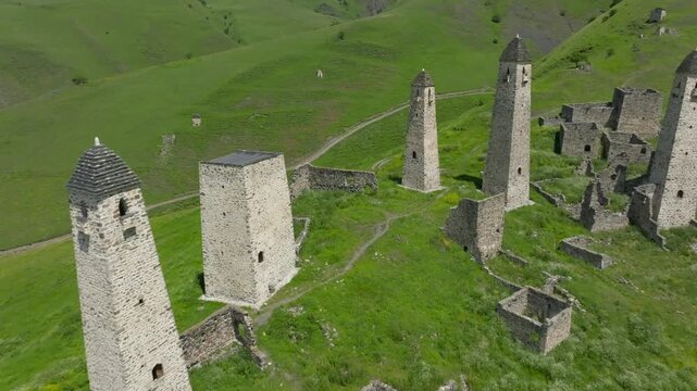 Drone footage of the medieval Erzi tower complex with stone watchtowers and ruins on green alpine hills, Dzheyrakhsky District, Ingushetia, Russia