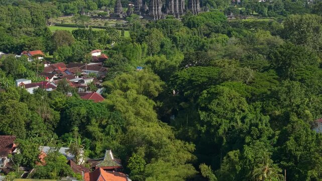 Aerial view of Prambanan Temple and traditional village houses nestled among lush tropical trees and green vegetation in Kecamatan Prambanan, Daerah Istimewa Yogya, Indonesia.