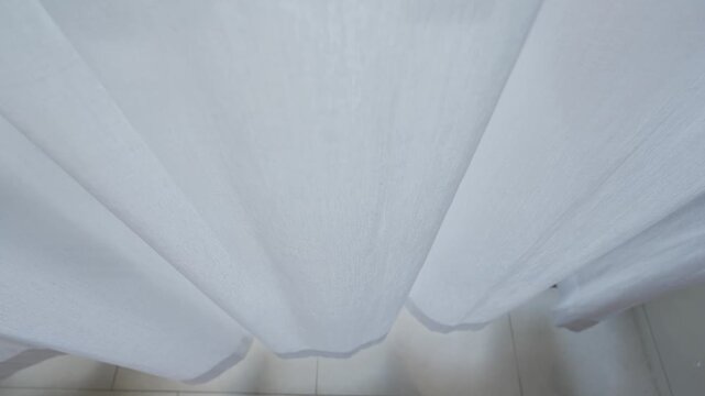 Wind blows the curtain or sways blind in the house or hotel bedroom living room. Sunny day with sun shines through the tulle through the window calm quiet morning curtain texture background.