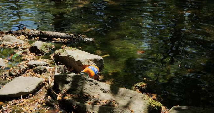 Urdorf, Switzerland, April 29. Discarded orange soda can polluting a pristine forest riverbank and stuck between rocks in a stream.