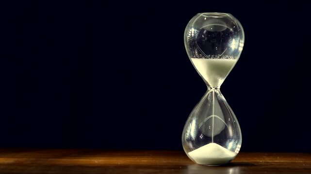 Hourglass with White Sand on Wooden Table Against Black Background