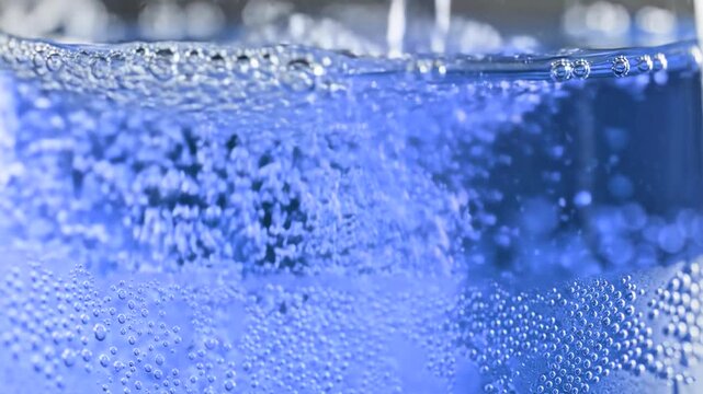 A high-quality macro video of vibrant blue carbonated liquid being poured, featuring dense rising bubbles and fizz. Ideal for soft drink marketing.