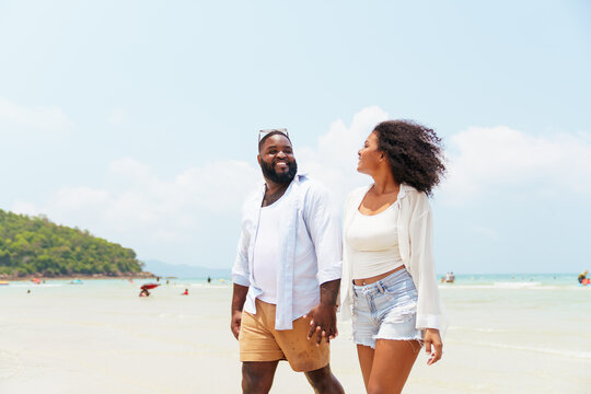 Happy African couple holding hands and walking on the beach
