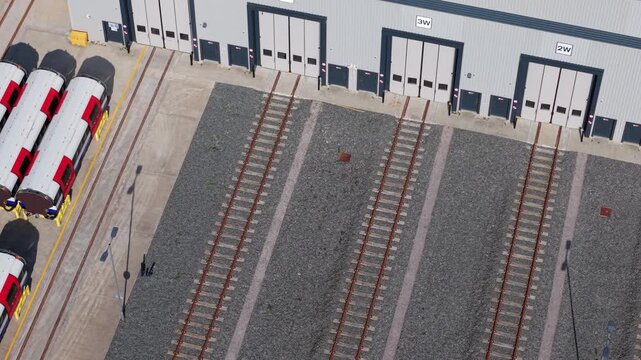 Aerial view of the Siemens Mobility train factory with red and white carriages parked on tracks outside industrial hangar doors in Goole, England, United Kingdom.