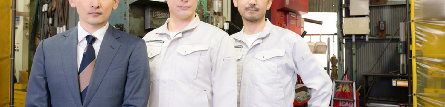 工場の製造業の現場で働く作業着とスーツの営業マン3人チームのポートレート　中小企業のカメラ目線の真剣な表情の顔無しのバナー