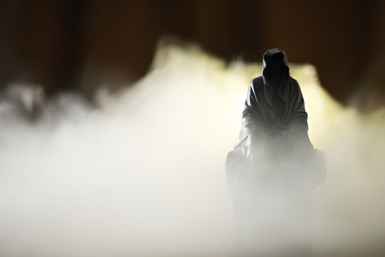 Mystical hooded figure surrounded by ethereal fog in a dark, mysterious setting