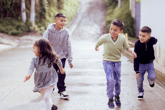 Hispanic children running down the street playing and smiling