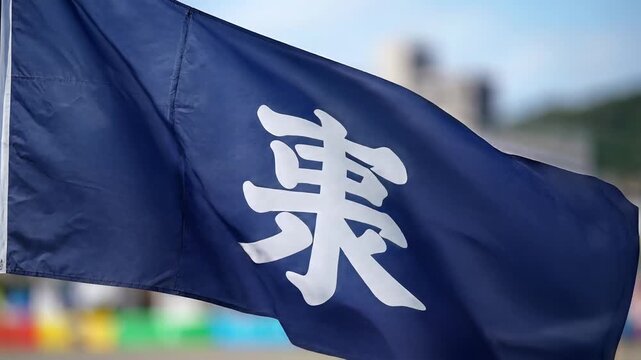 Closeup of a dark blue flag with a white Japanese Kanji character fluttering in the wind.