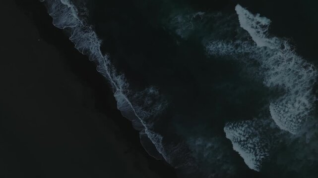 Top down aerial footage of ocean waves breaking on black volcanic sand at Khalaktyrsky Beach, Kamchatka Krai, Russia, dramatic seascape background