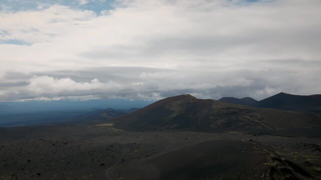 Wide aerial view of Tolbachinsky Dol volcanic desert with dark lava fields, cinder cones, and layered clouds over Kamchatka Krai, Russia