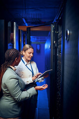 Fototapeta na wymiar Women, tablet and team with review in server room with cybersecurity, system check or collaboration. Programmer, tech and advice with smile for programming, maintenance or IT solution at data center