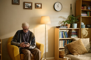 Fototapeta premium Senior Caucasian man using smartphone while sitting at home, managing digital communication and daily tasks. Useful for retirement planning, telehealth, mobile banking marketing