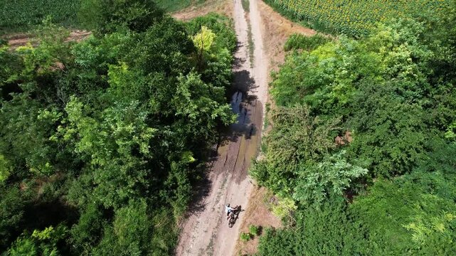Aerial view of cyclists riding on a dirt path through lush green forest and dry fields near Solnitsata in Provadia, Varna, Bulgaria.