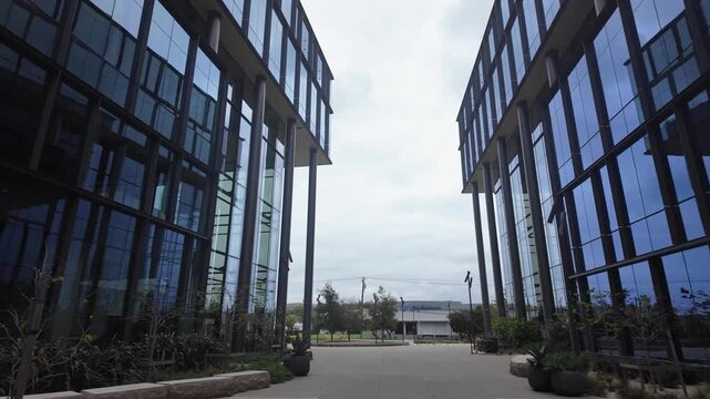 Slow forward movement through an empty courtyard between two contemporary glass buildings, which are part of a medical laboratory campus in South San Francisco, California on a cloudy day