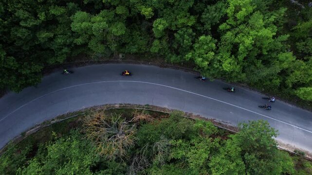 Aerial view of cyclists riding on a winding asphalt road through a dense green forest in Provadia, Varna, Bulgaria.
