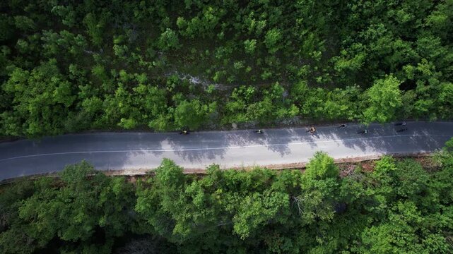 Aerial view of motorcyclists riding on a winding asphalt road through a dense green forest near Provadia, Varna, Bulgaria.