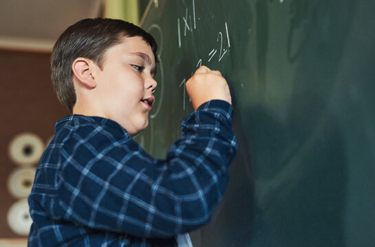 Boy, child and writing on chalkboard in classroom for math lesson, solution and scholarship at school. Kid, problem solving and notes for education, development and learning with equation at academy