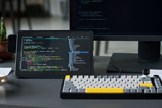 Close up of coding workspace displaying software development on tablet and monitor, showing programming and debugging. Useful for app development, IT training, tech marketing