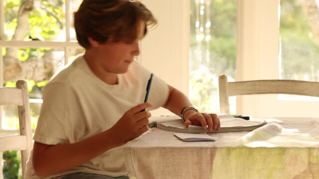 12 year old boy doing homework at kitchen table at sunset