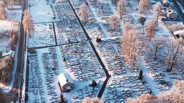 Snow blankets the cemetery with many gravestones and trees