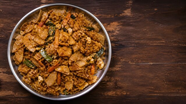 Sri Lankan kottu roti served in a metal plate on rustic dark wood with copy space. Useful for street food menus, restaurant ads, travel food, and takeout campaigns.