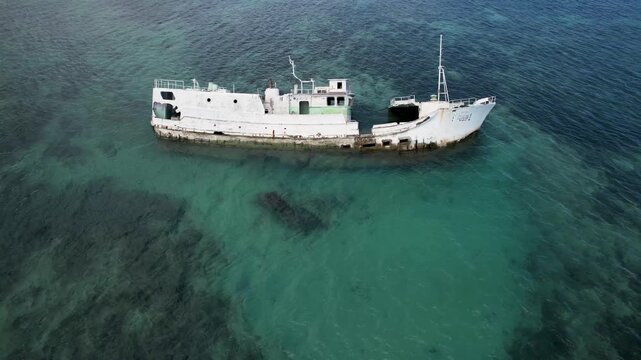 Aerial view of a white shipwreck resting in clear turquoise waters near a coral reef in Wewak, East Sepik Province, Papua New Guinea.