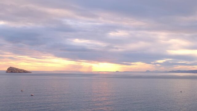 Sunset view over Cala Tio Ximo and Benidorm island. Tranquil winter sea, soft sunset glow, peaceful view of small island near Benidorm. Quiet natural beauty, no people, only sea and sky.