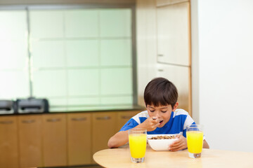 School-age boy in striped shirt sitting at kitchen table eating cereal from white bowl, copy space © wavebreak3