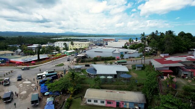 Aerial view of the town center with buildings, streets, people walking, and the coastline under a cloudy sky in Wewak, East Sepik Province, Papua New Guinea.