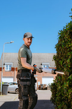Man using hedge trimmer while working in suburban neighborhood