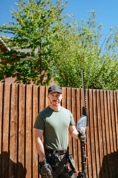 Man holding hedge trimmer standing by wooden fence in garden