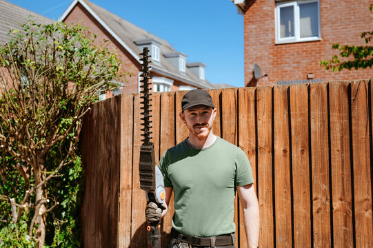 Gardener holding hedge trimmer near wooden fence