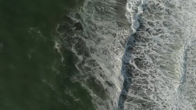 Top down aerial footage of ocean surf and white sea foam rolling onto the dark sand of Khalaktyrsky Beach, Kamchatka Krai, Russia, natural seascape texture