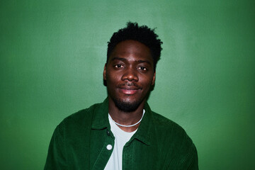Fototapeta premium Portrait of young Black man looking at camera against green background, conveying confidence and authenticity. Ideal for diversity marketing, personal branding, profile use